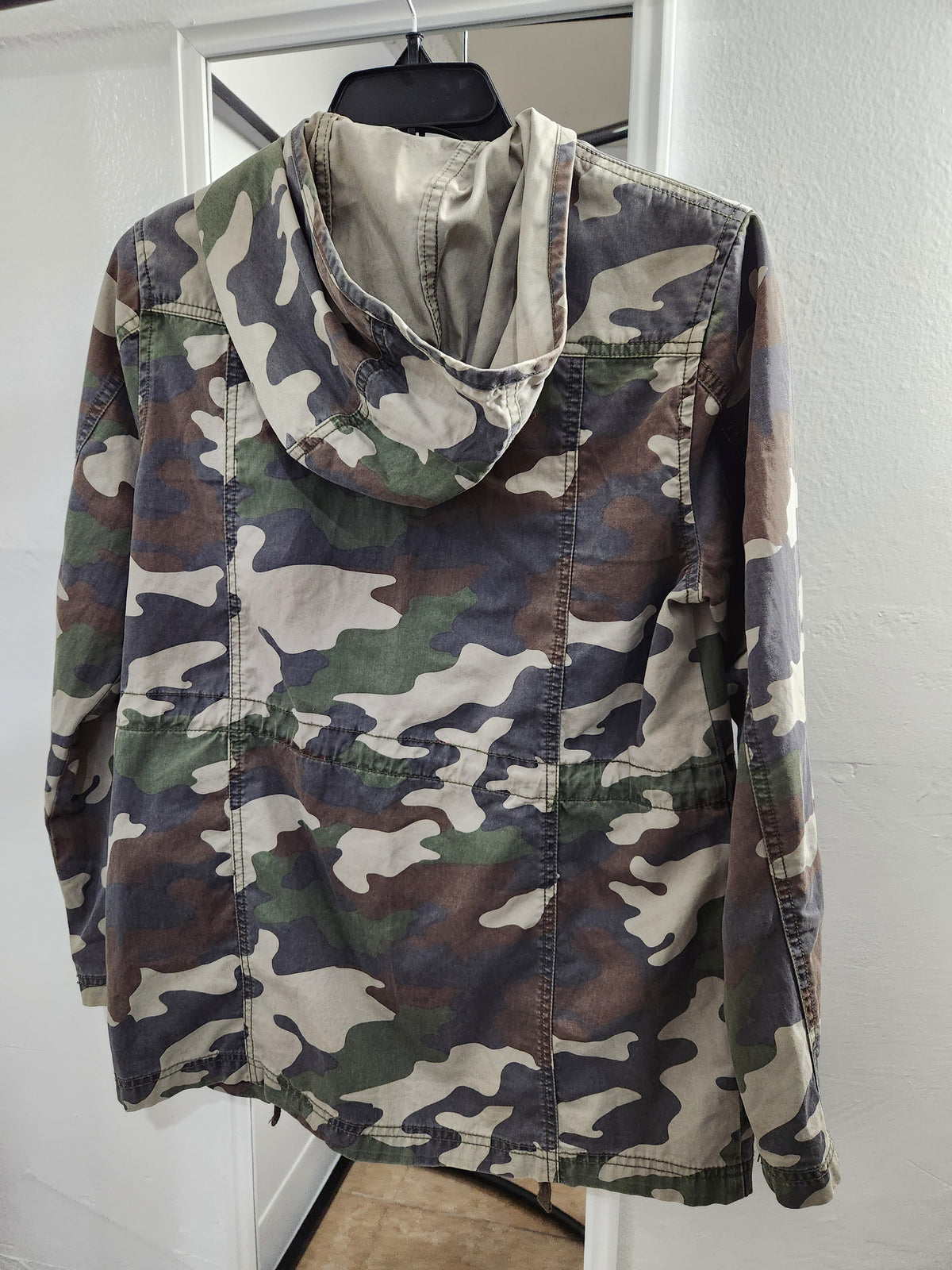 A hooded camouflage jacket hanging on a black hanger against a white door and wall.