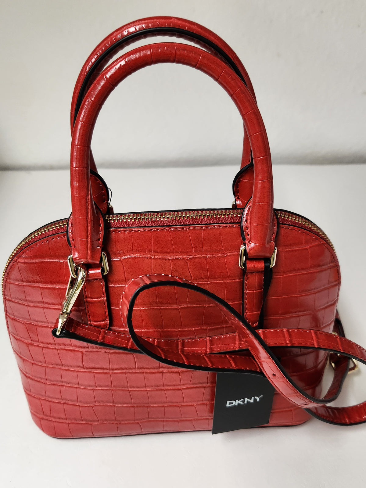 A red crocodile-embossed leather handbag with double top handles, a detachable shoulder strap, and a black DKNY brand tag, photographed against a plain light background.
