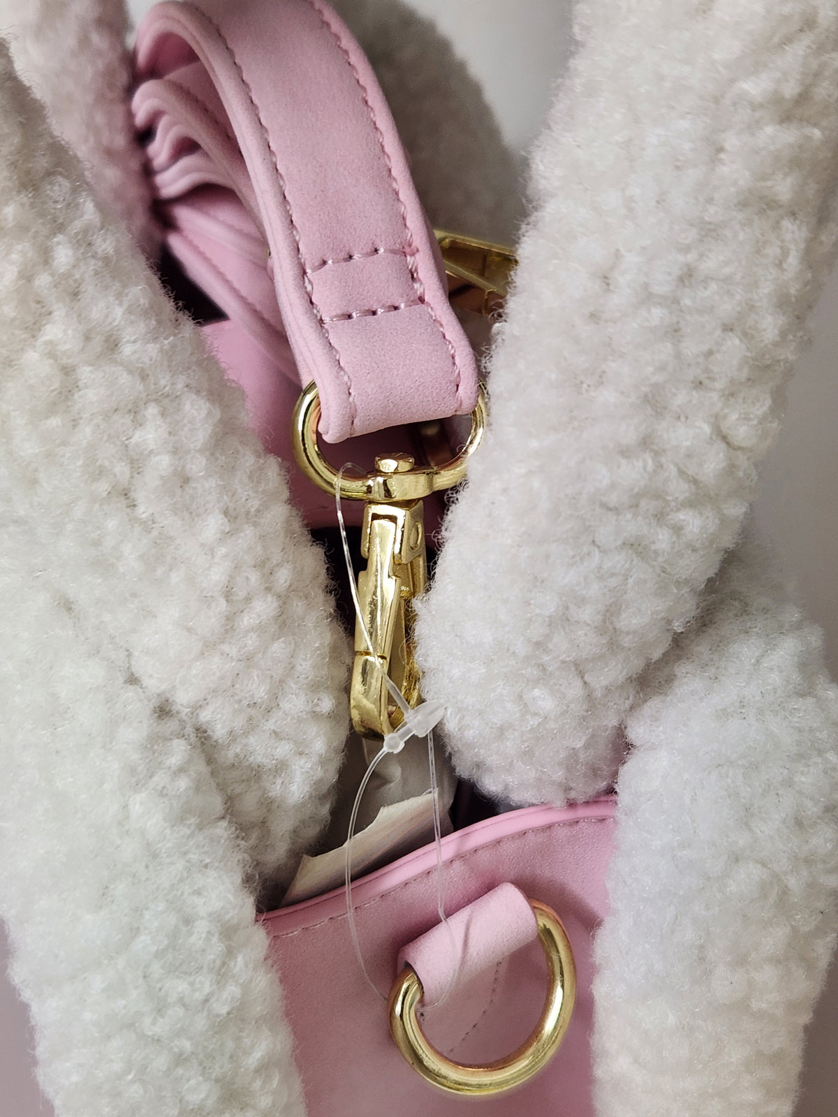 Close-up of a pink handbag with a soft white sherpa or fleece lining, featuring gold-tone metal hardware and a pink strap.