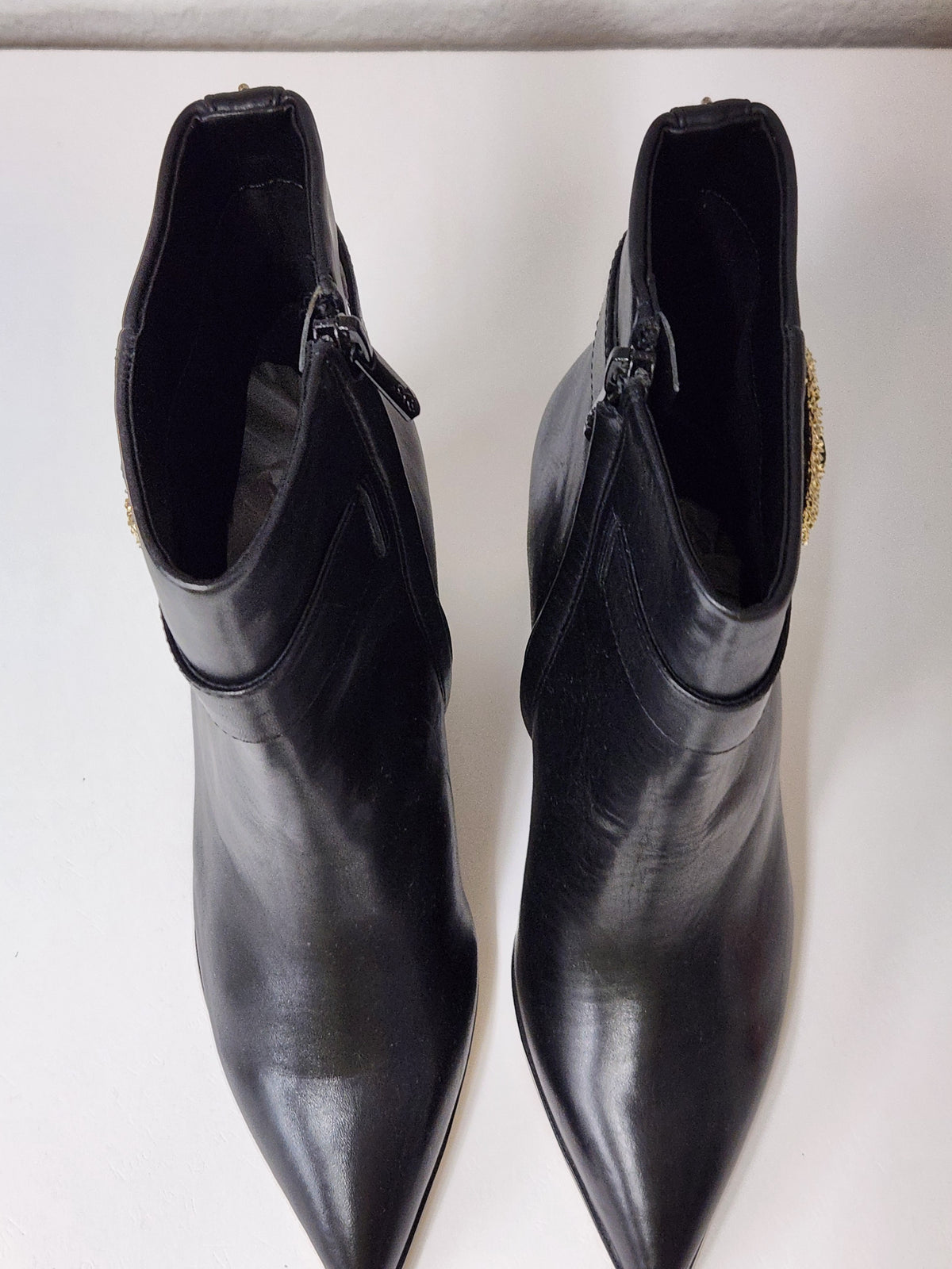 A pair of black leather pointed-toe ankle boots with side zippers and small gold decorative accents near the collar, shown on a plain light background.