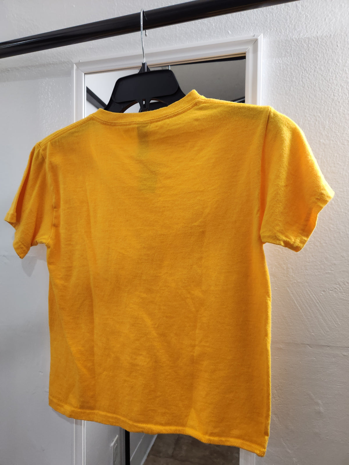 A bright yellow short-sleeve t-shirt hanging on a black hanger against a white wall.