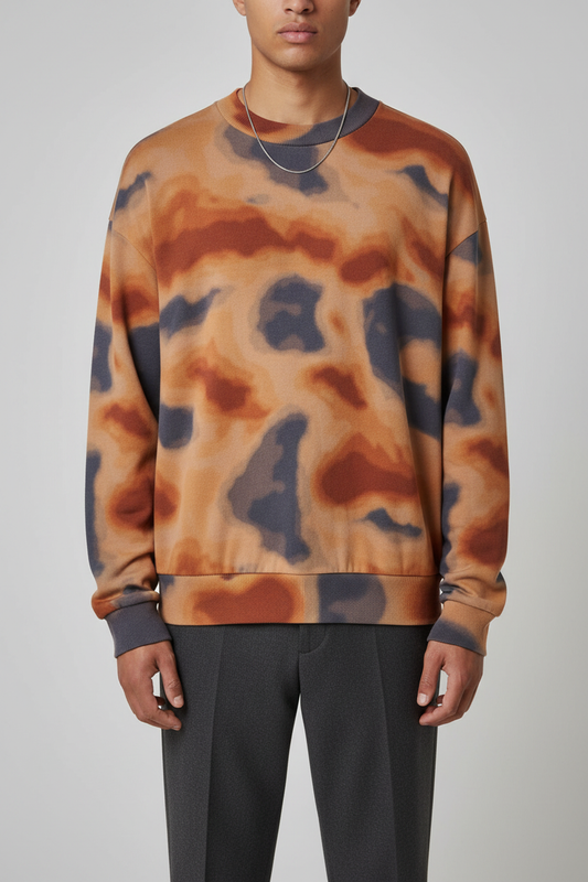 A man wearing a crewneck sweatshirt with an abstract wavy pattern in orange, brown, and dark gray, paired with dark gray trousers, against a light gray studio background.