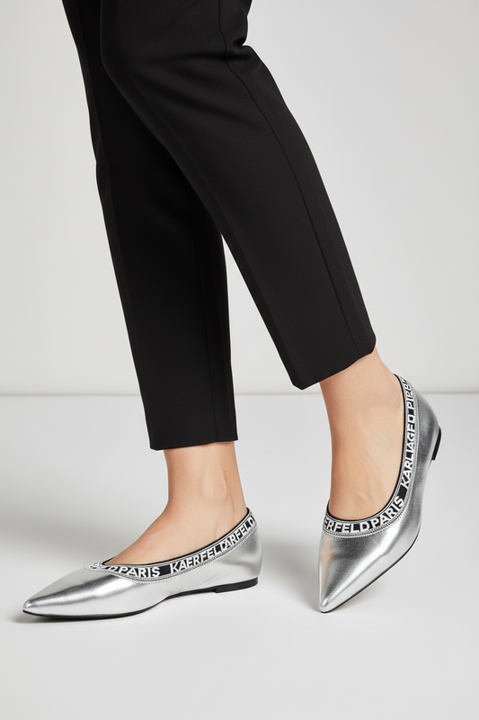 A person wearing black cropped pants and metallic silver pointed-toe flats with a black and white 'KANSAS CITY' text band around the collar, shown against a light gray studio background.