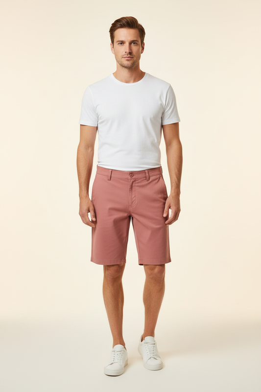 A man modeling a white crew-neck t-shirt and dusty rose pink shorts, paired with white sneakers, against a solid light beige background.