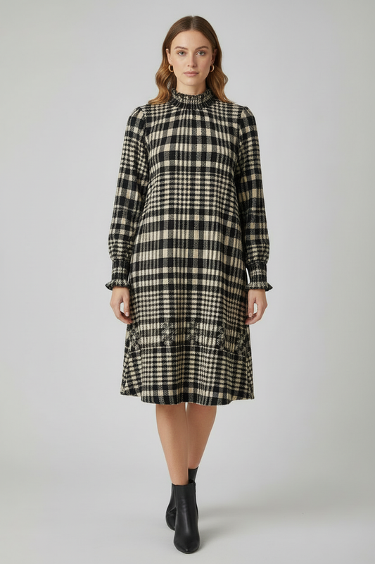 A woman modeling a long-sleeve black and beige plaid midi dress with a high gathered neckline and ruffled hem, paired with black ankle boots, against a light gray studio background.