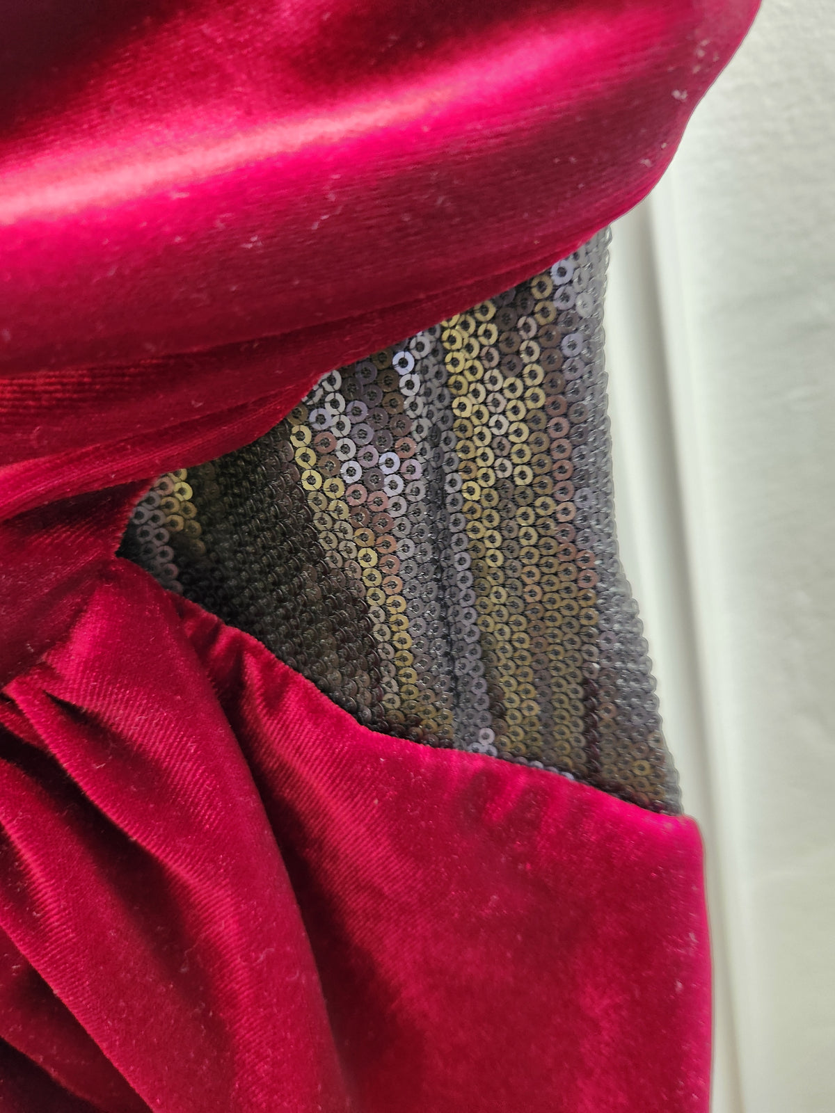 Close-up of a garment featuring a deep magenta velvet fabric paired with a textured panel of metallic gold and silver sequins.