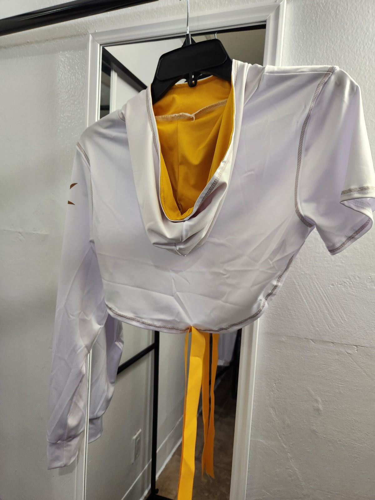 A white short-sleeve crop top with a deep V-neck and a bright yellow inner lining, hanging on a black hanger in front of a white door.