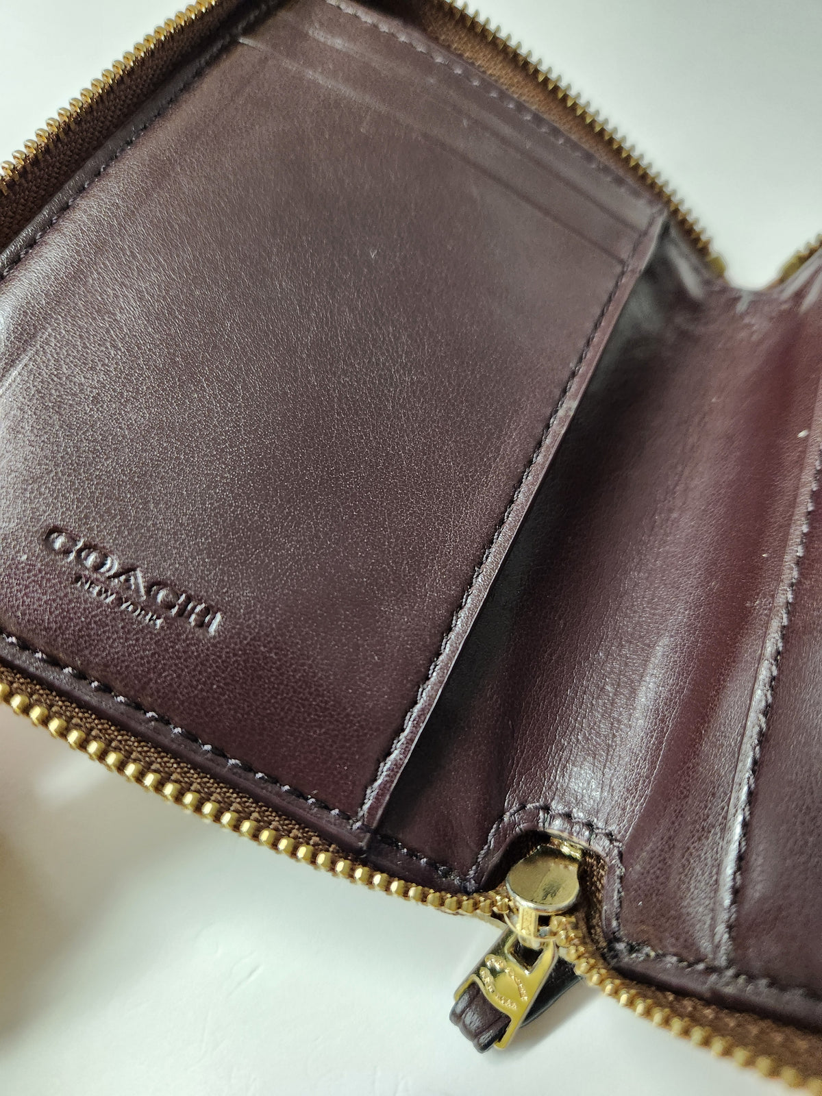 Close-up of an open Coach zip-around wallet in dark brown leather, showing interior card slots, stitching, and a gold-tone zipper pull with the Coach logo