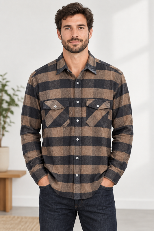 A man wearing a brown and black buffalo plaid long-sleeve button-down flannel shirt, paired with dark blue jeans, standing in a bright indoor setting.