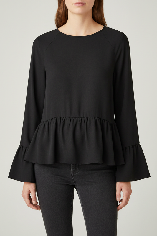 A woman wearing a black long-sleeve blouse with a peplum waist and flared cuffs, paired with dark gray pants, against a light gray studio background.