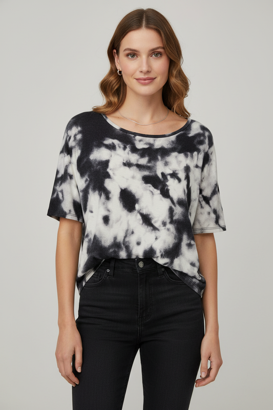 A woman modeling a black and white tie-dye short-sleeve top with black jeans against a light gray studio background.