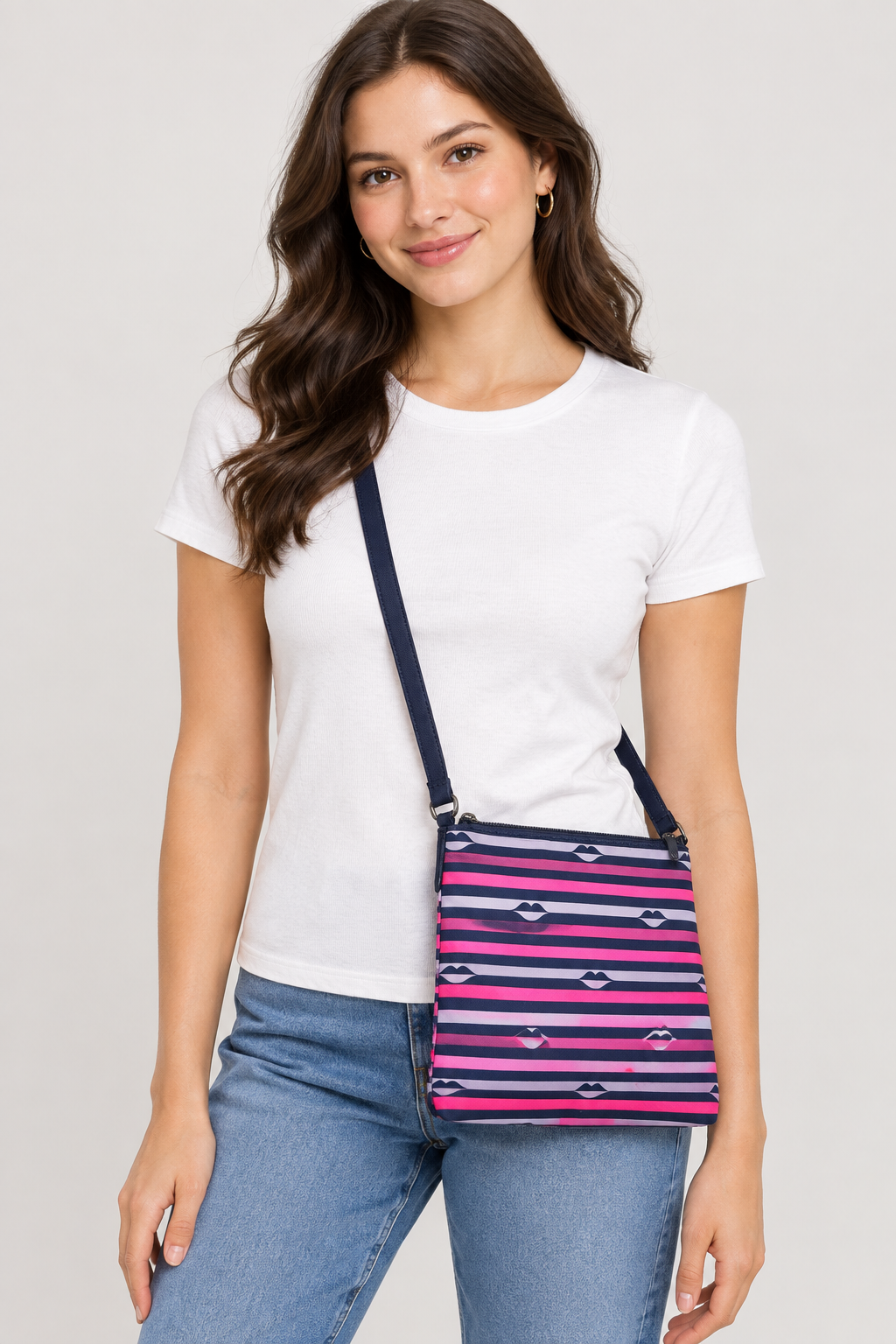 A woman wearing a white t-shirt and blue jeans models a small crossbody bag with a pink, navy, and white striped pattern featuring small bow tie motifs.