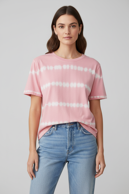 A woman modeling a light pink short-sleeve t-shirt with white tie-dye horizontal stripes, paired with light-wash blue jeans, against a solid light gray background.