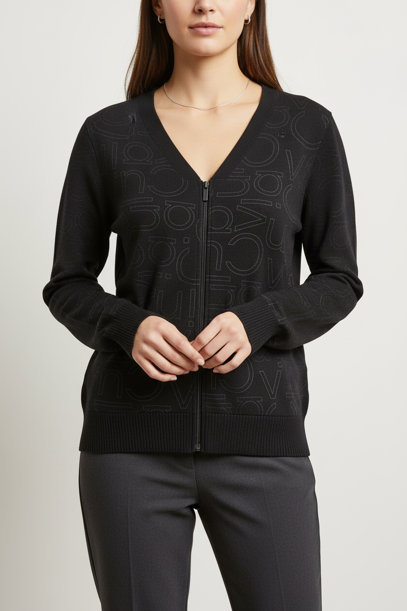 A woman wearing a black zip-up V-neck sweater with an all-over tonal monogram pattern, paired with dark trousers, against a light gray studio background.