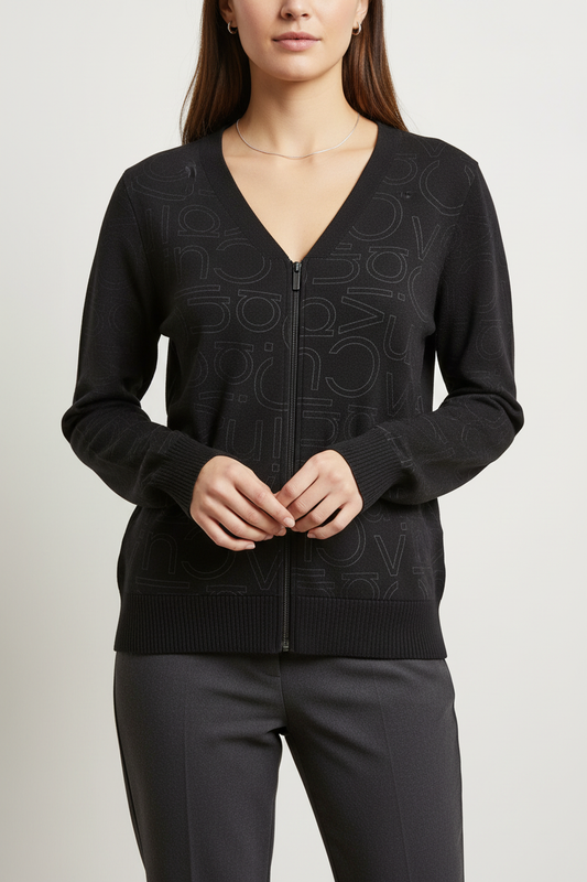 A woman wearing a black zip-up V-neck sweater with an all-over tonal monogram pattern, paired with dark trousers, against a light gray studio background.