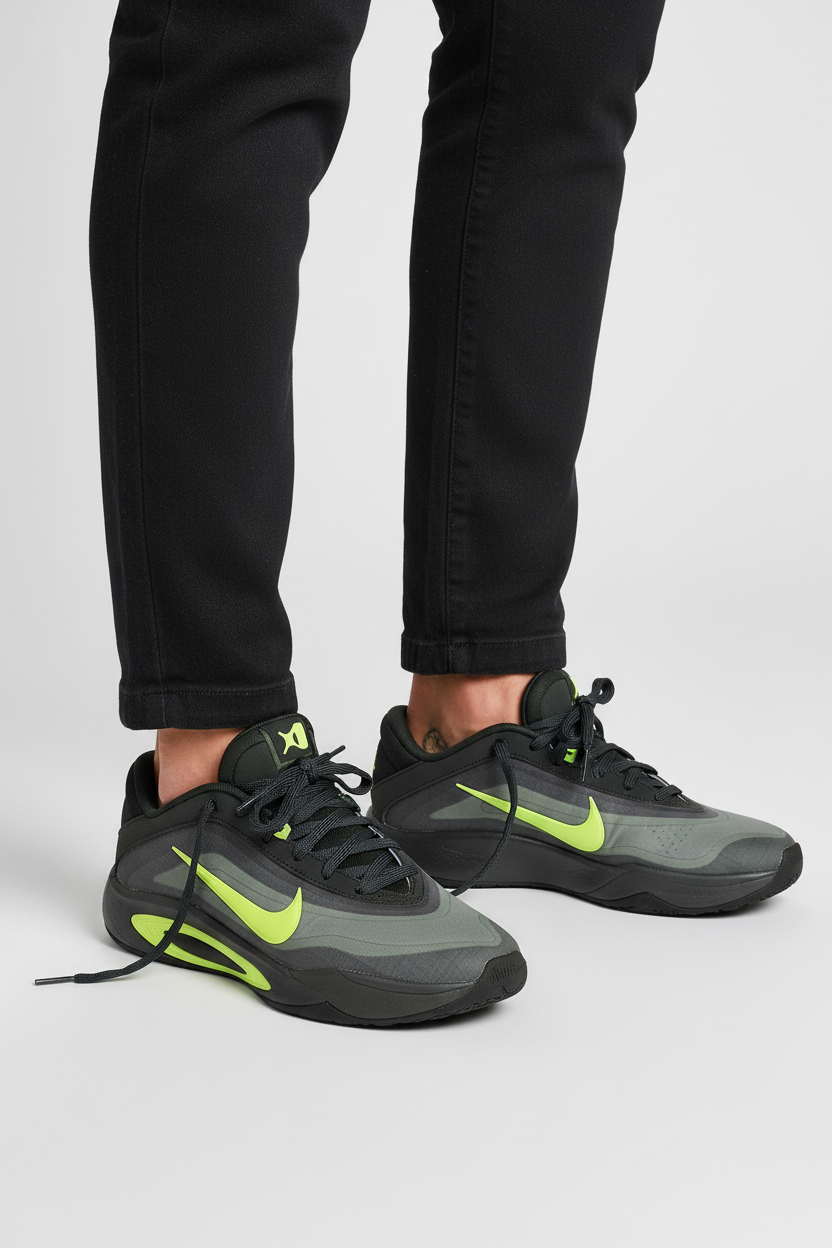 A pair of Nike low-top sneakers in dark gray and black with bright neon yellow-green accents, shown on a model wearing black pants against a light gray studio background.
