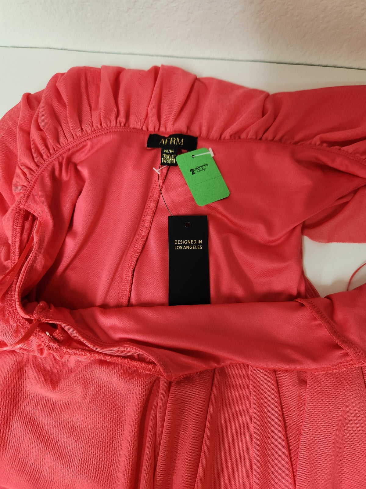 A coral pink off-the-shoulder long-sleeve top by AF RM, featuring a black 'Designed in Los Angeles' tag and a green resale tag, laid flat on a white surface.