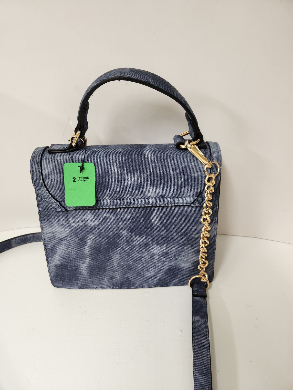 A small structured handbag in a mottled blue-gray material with a top handle, gold-tone hardware, a detachable chain strap, and a bright green hangtag, photographed against a plain off-white background.