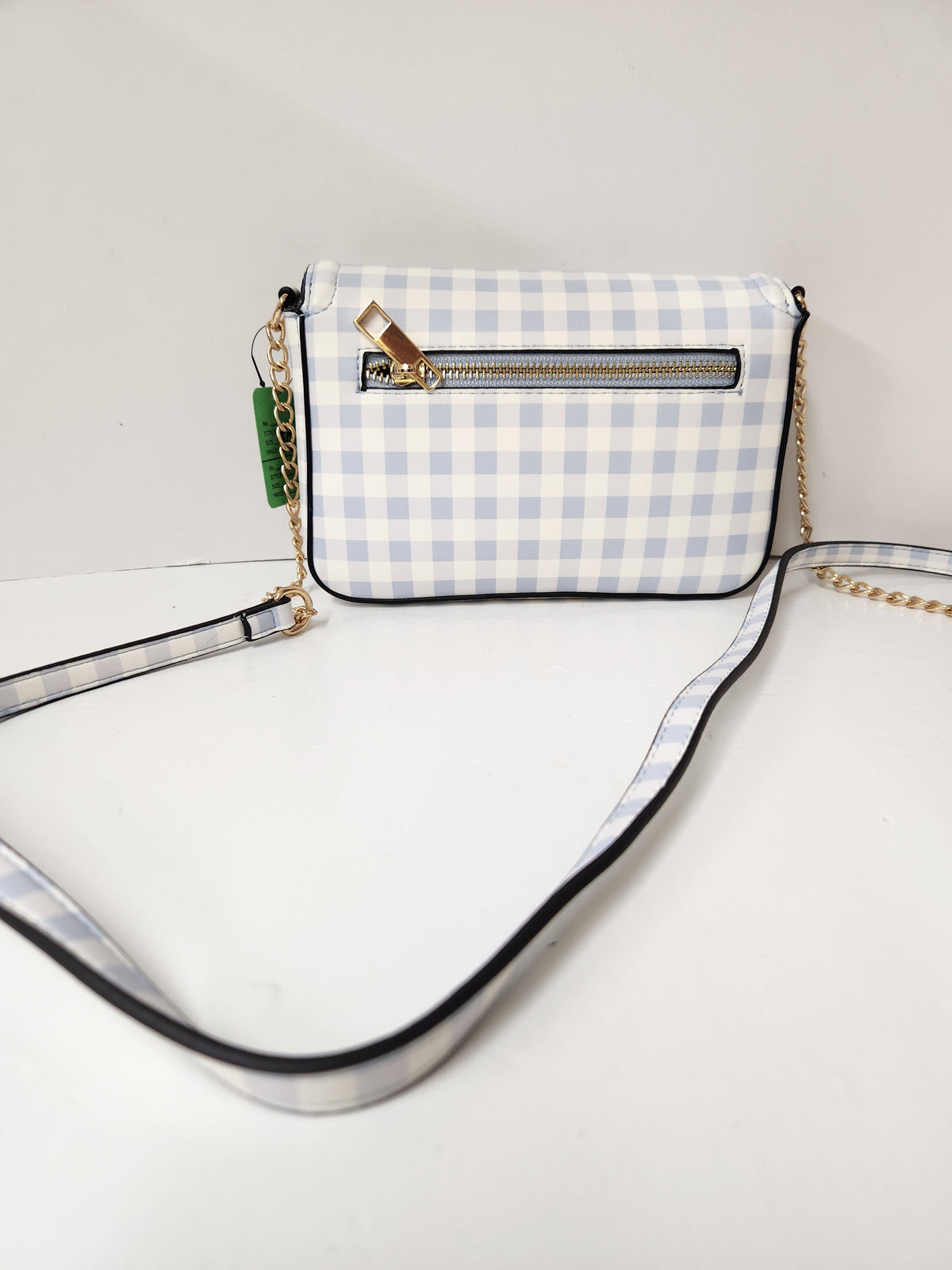 A small crossbody bag with a light blue and white gingham check pattern, featuring a front zip pocket, gold-tone hardware, and a long strap with black trim and a gold chain.