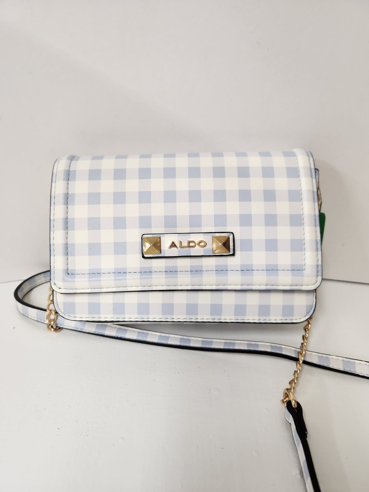 A light blue and white gingham check crossbody bag with a gold-tone ALDO logo plate on the front flap, resting on a white surface.