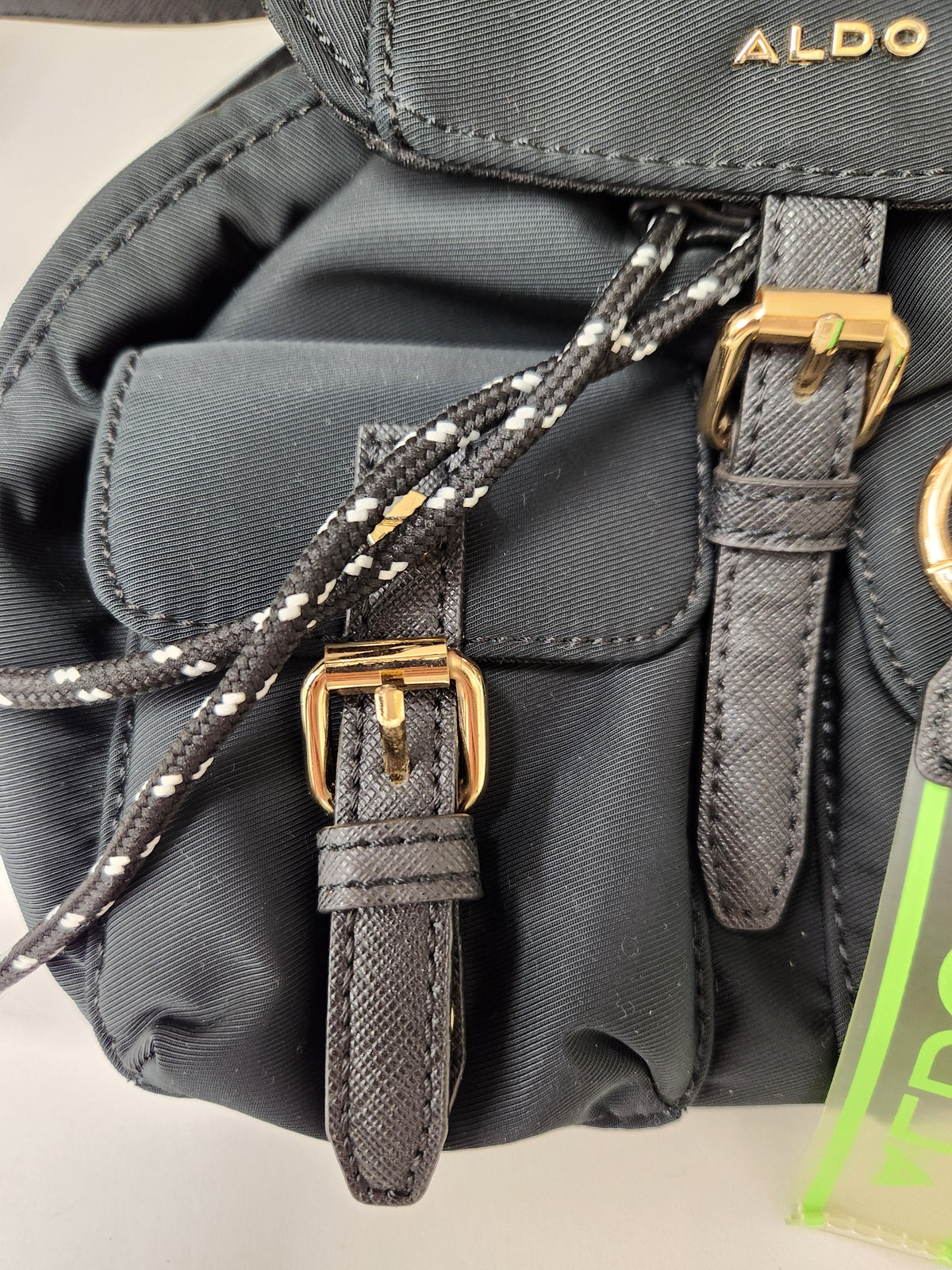Close-up of a black nylon Aldo handbag with gold-tone hardware, a braided black-and-white drawstring, and a visible Aldo logo on the flap.