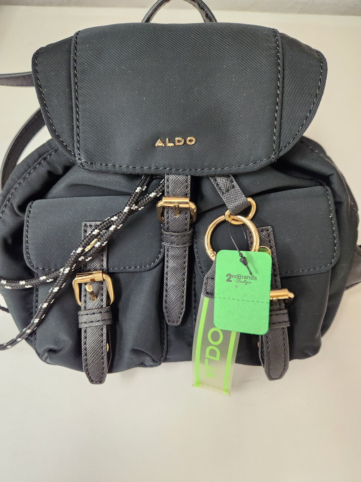 Close-up of a black nylon Aldo handbag with gold-tone hardware, a braided black-and-white drawstring, and a visible Aldo logo on the flap.