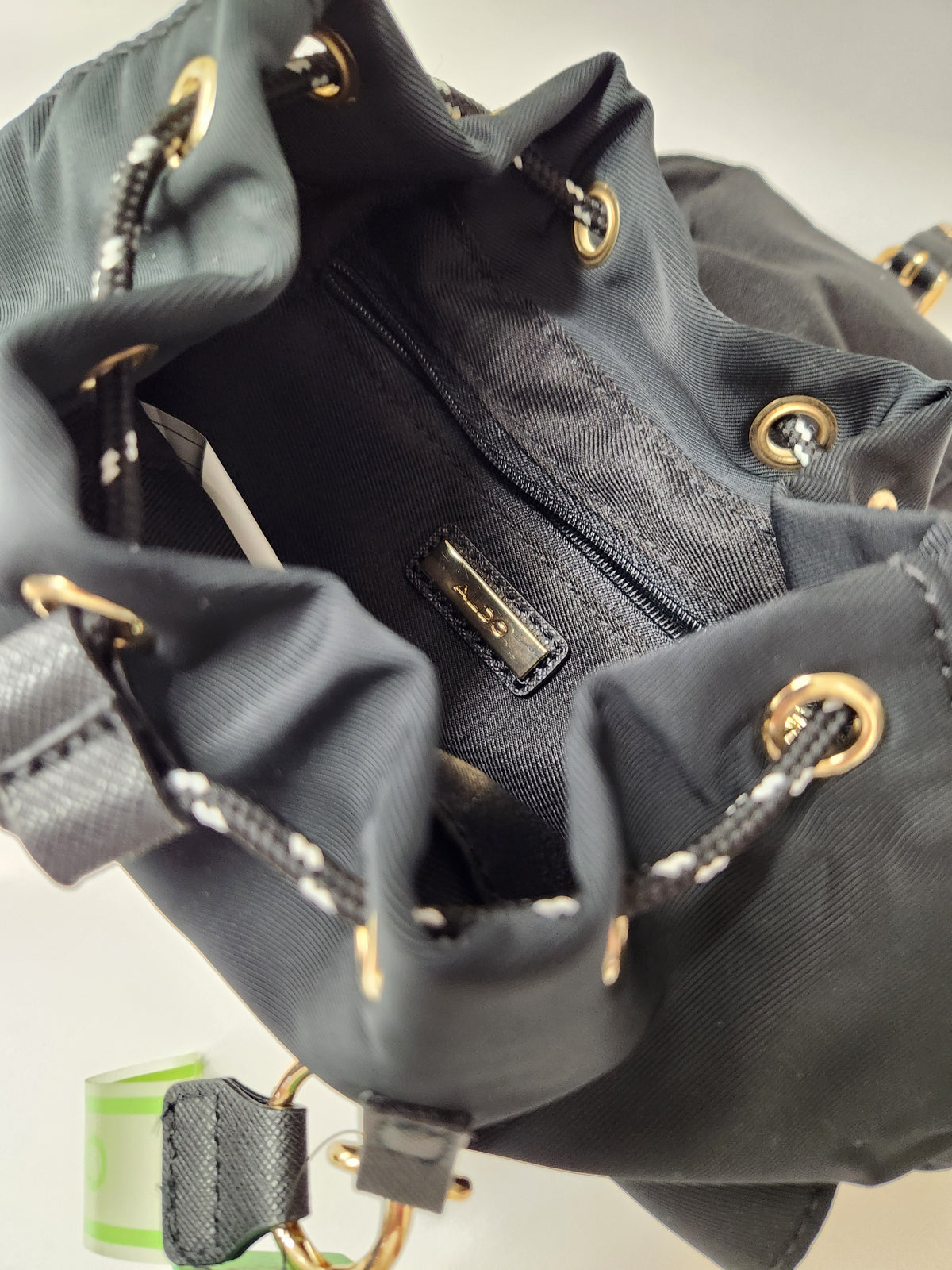 Close-up of a black nylon Aldo handbag with gold-tone hardware, a braided black-and-white drawstring, and a visible Aldo logo on the flap.