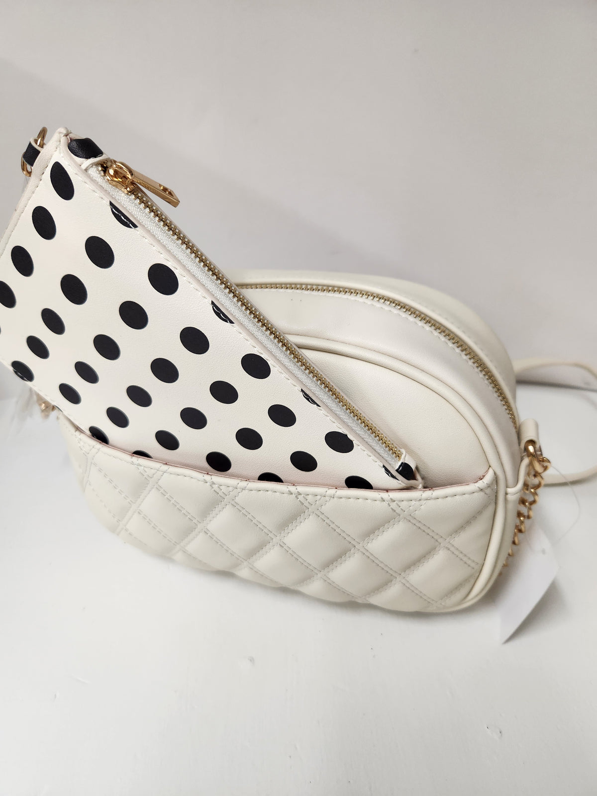 A cream-colored quilted crossbody bag with a black polka dot zippered pouch attached, shown on a plain white background.