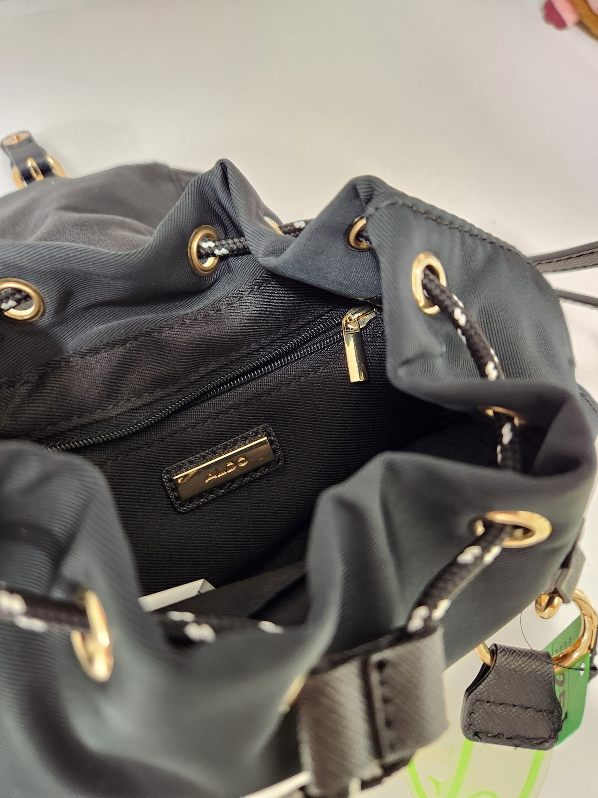 Close-up of a dark gray nylon drawstring bag with gold-tone hardware and a small metal brand plaque inside the opening.