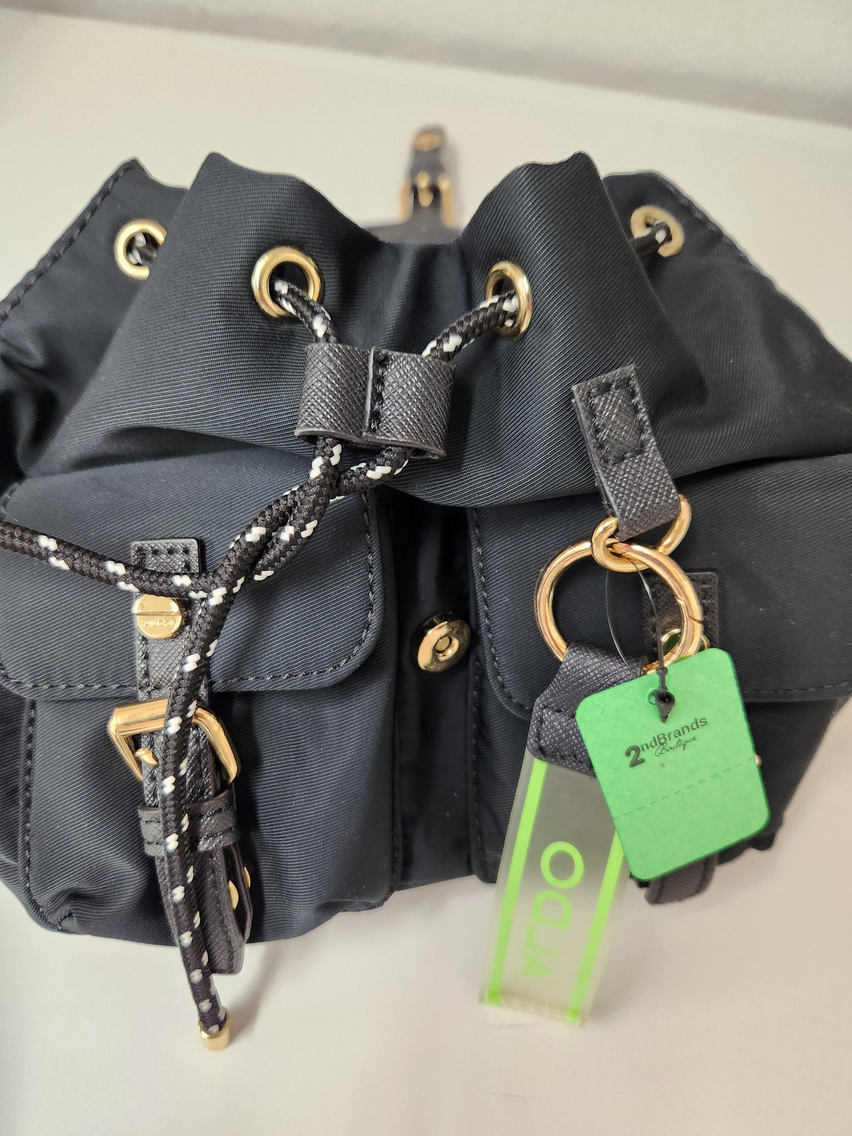  black Alor backpack with gold hardware against a light gray studio background.