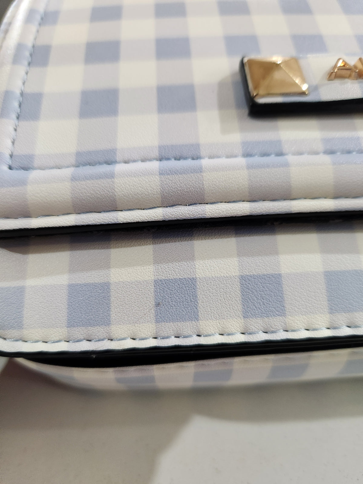 Close-up of a checkered bag or wallet in light blue and white faux leather with a gold-tone pyramid stud accent.