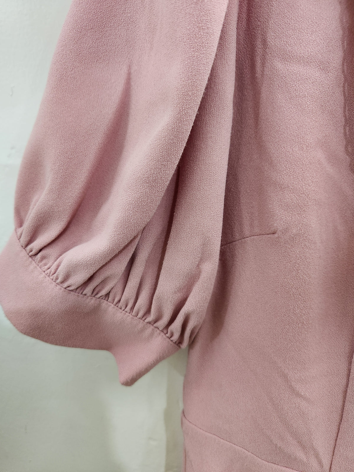 Close-up of a dusty pink garment with gathered puff sleeves and elastic cuffs, showing the soft textured fabric against a light neutral background.