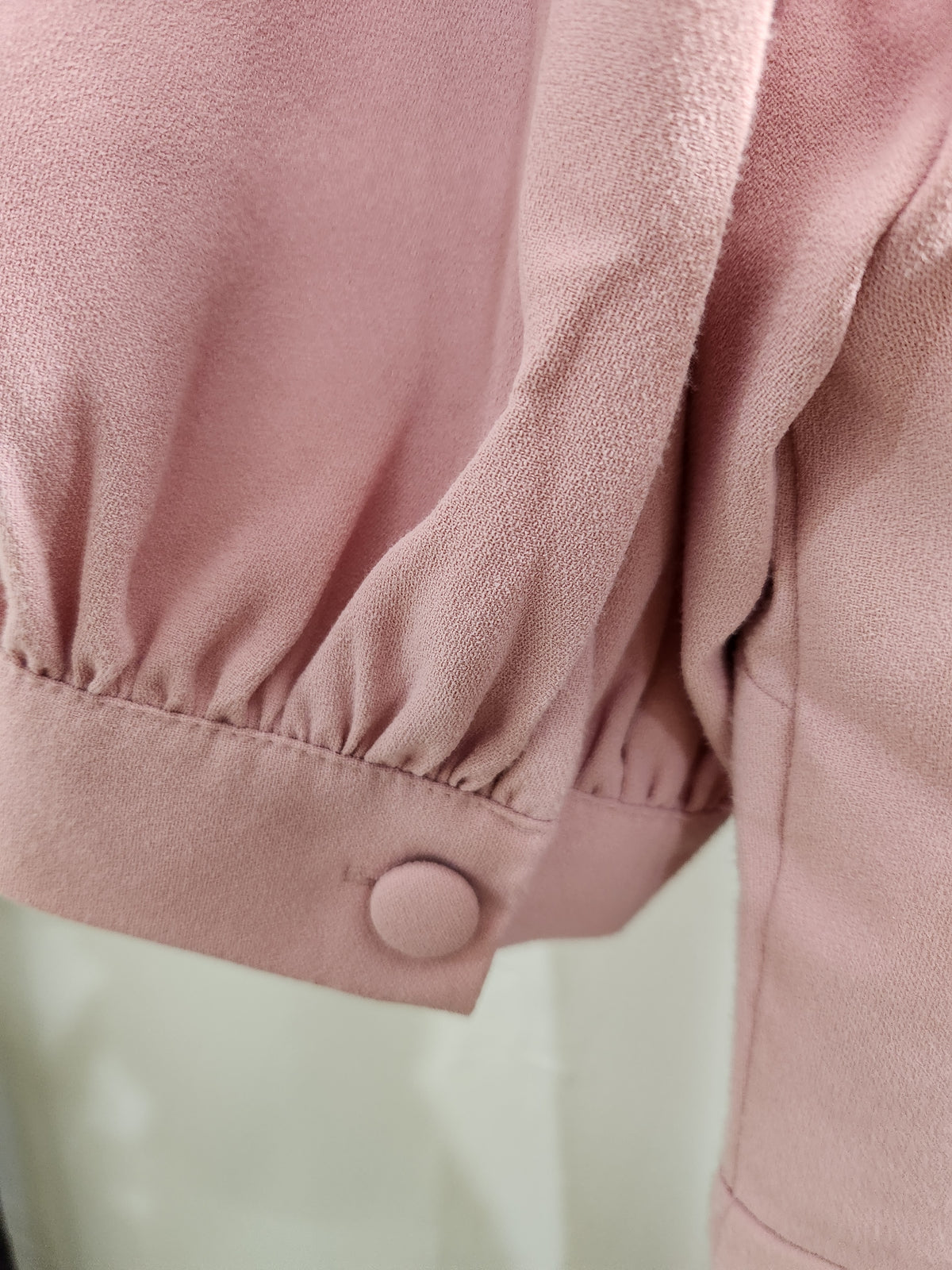 Close-up of a dusty pink garment with gathered elbow-length sleeves and a matching button detail on the cuff.