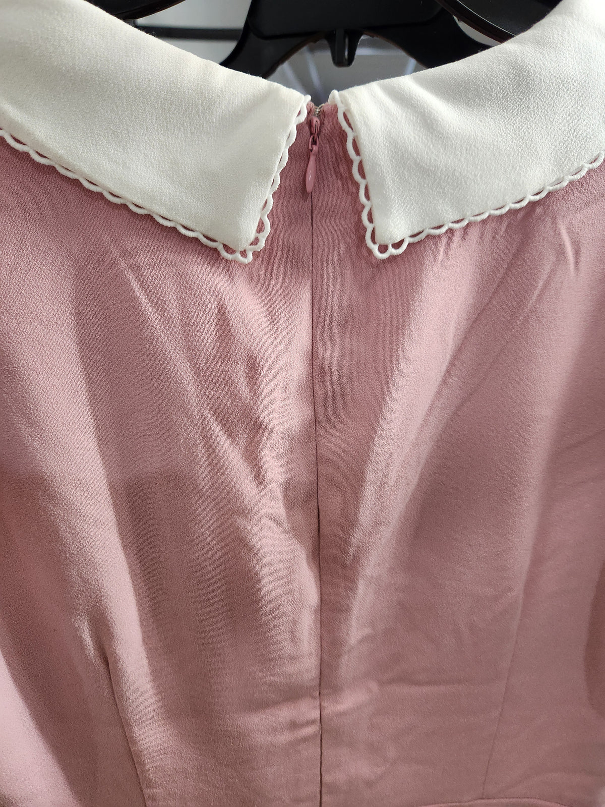 Close-up of a pink garment with a contrasting white pointed collar featuring scalloped edges and a central zipper.