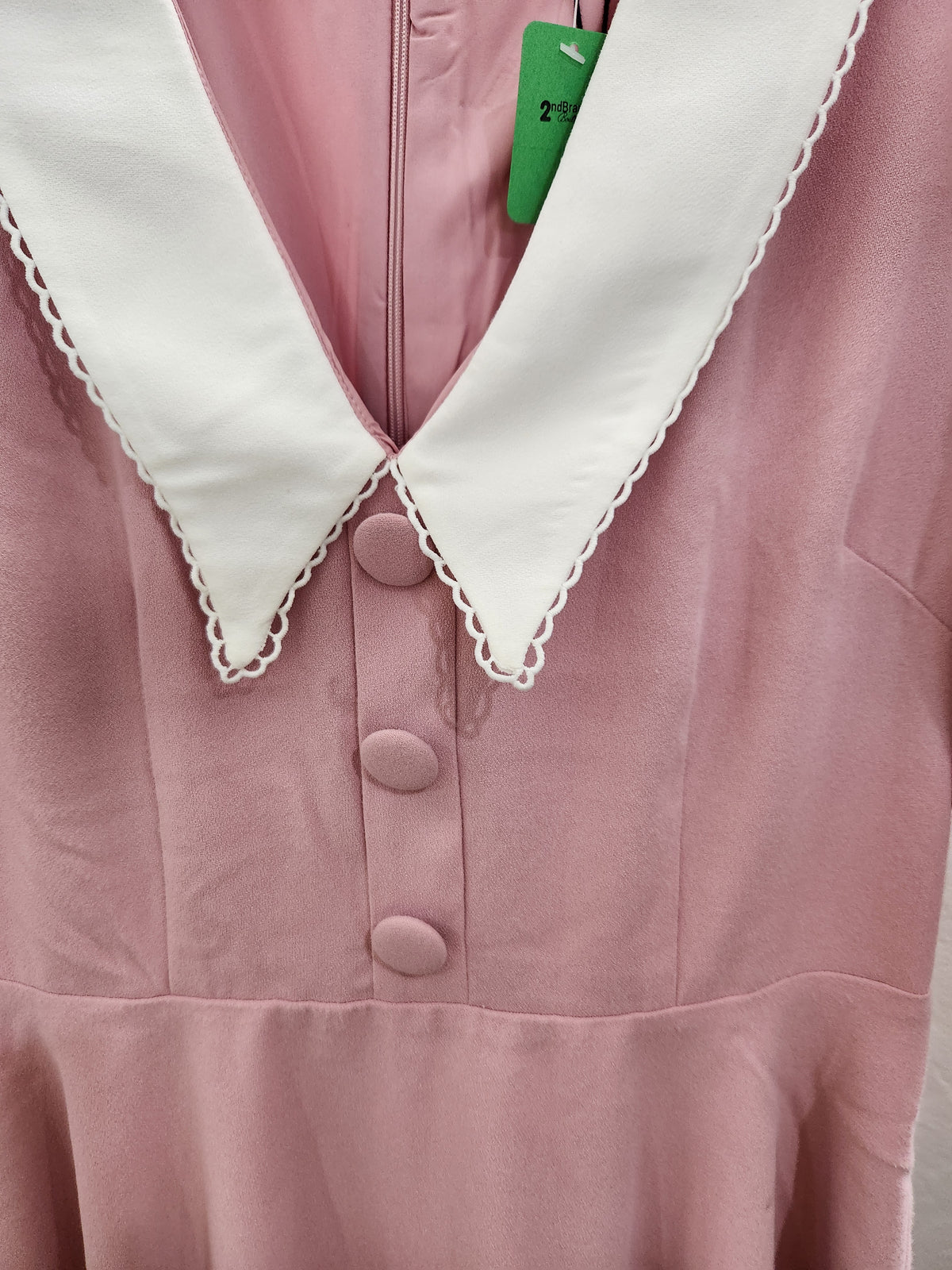 A close-up of a dusty pink dress featuring a contrasting white pointed collar with scalloped edges and matching pink buttons down the front.