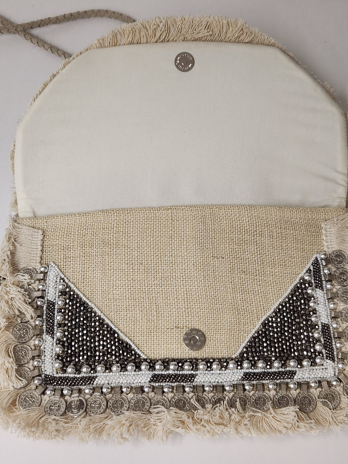 A handmade clutch bag made of natural burlap and cream fabric, decorated with silver coin fringe, beadwork, and a snap closure.