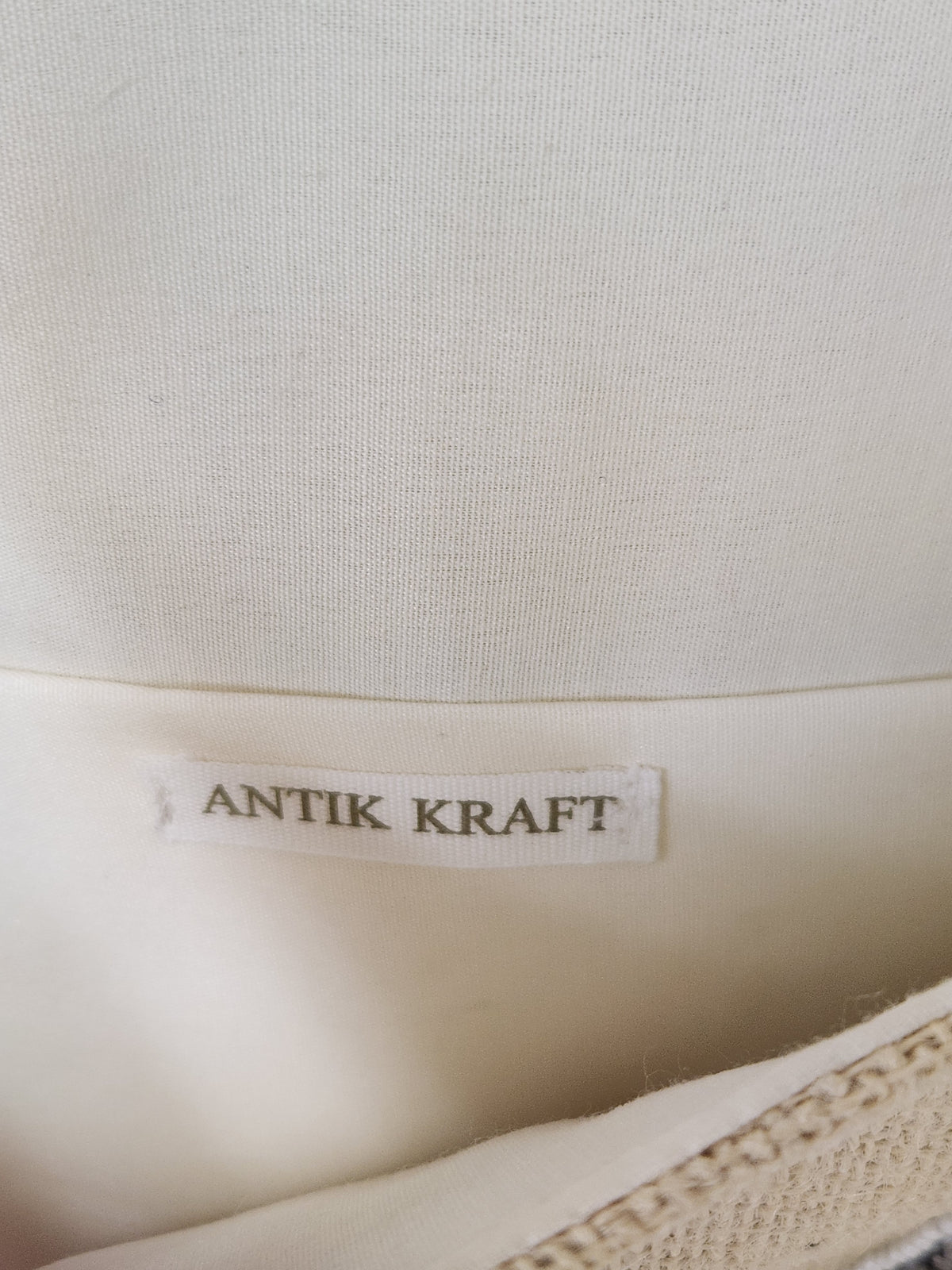 Close-up of a cream-colored fabric item showing a sewn-on label that reads 'ANTIK KRAFT'.