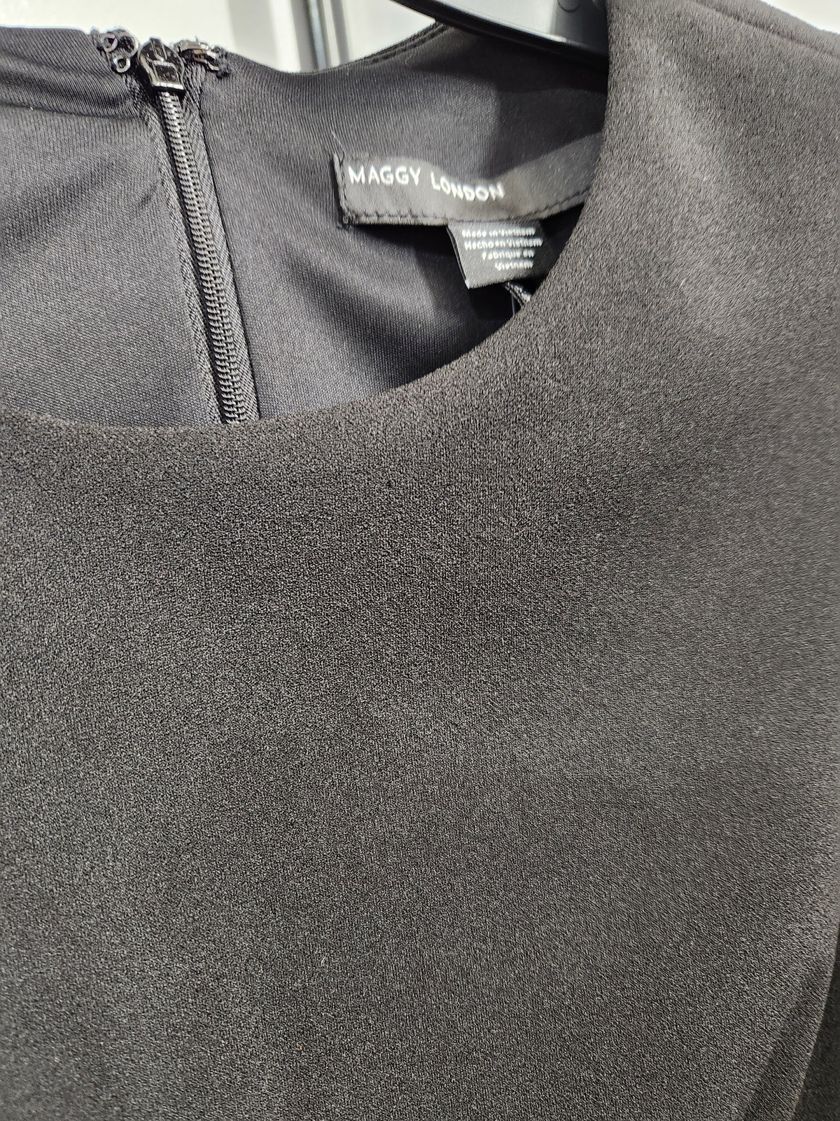 Close-up of a dark gray textured faux fur or suede-like top by Maggy London, showing a round neckline, zipper closure, and brand label.