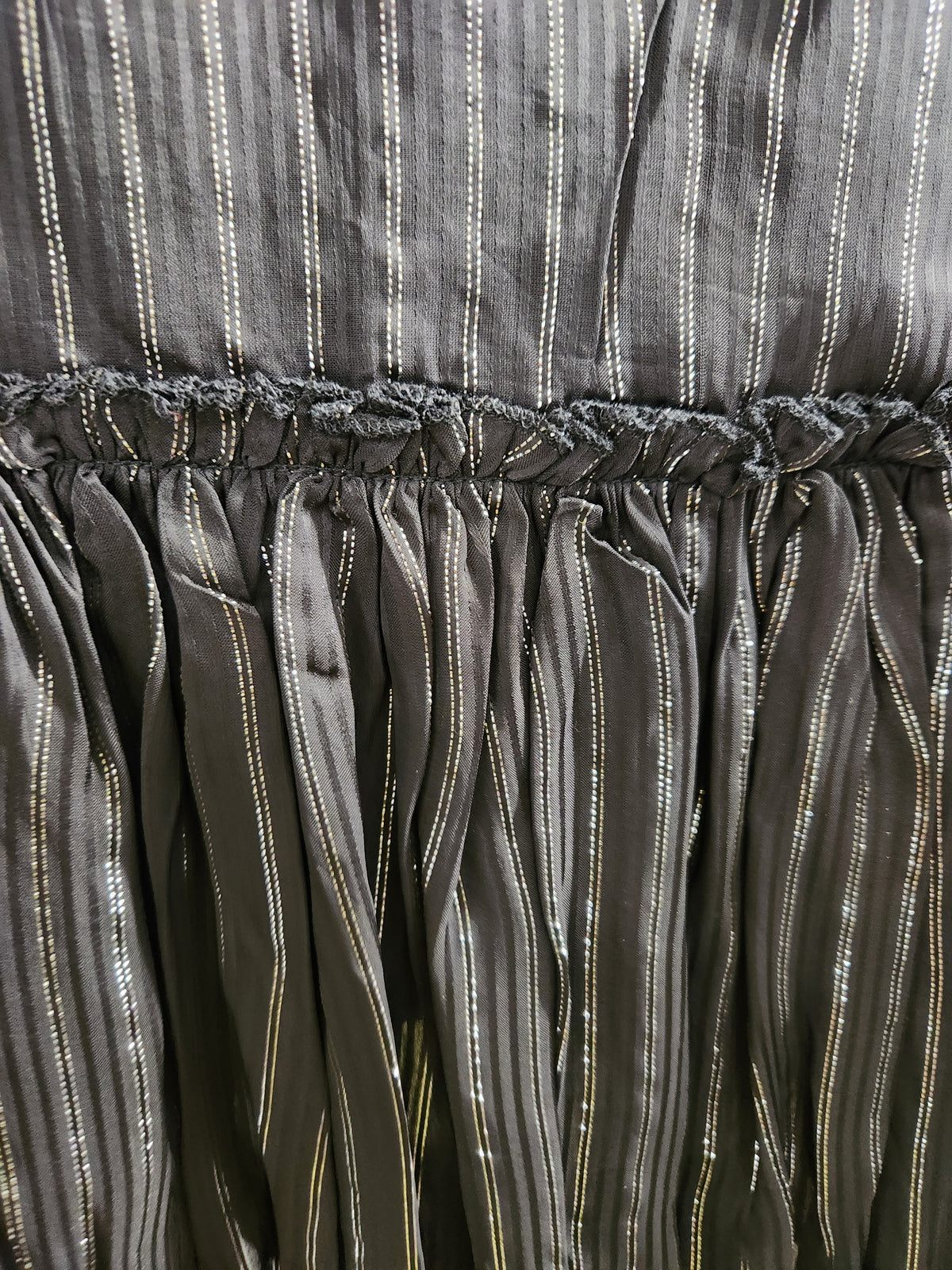Close-up of a dark gray or charcoal fabric with vertical metallic gold stripes and a gathered elastic waistband.