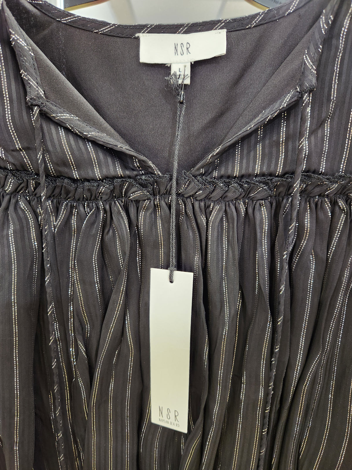 Close-up of a dark gray hooded top with thin vertical metallic gold stripes, featuring a smocked chest and a hanging white KSR brand tag.