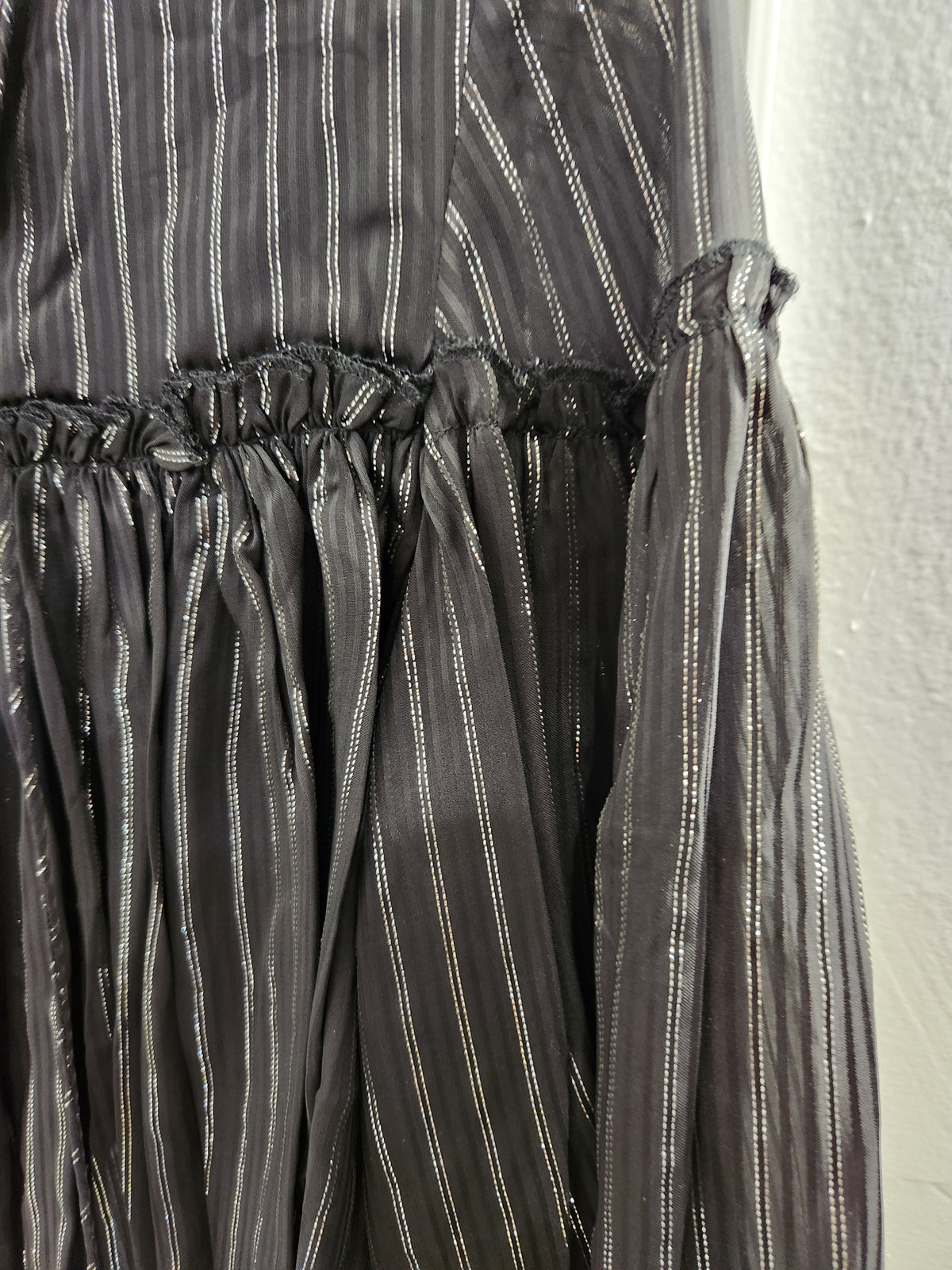 Close-up of a dark gray or black sheer fabric with vertical metallic silver stripes, featuring a gathered elastic waistband and ruffled sleeves.