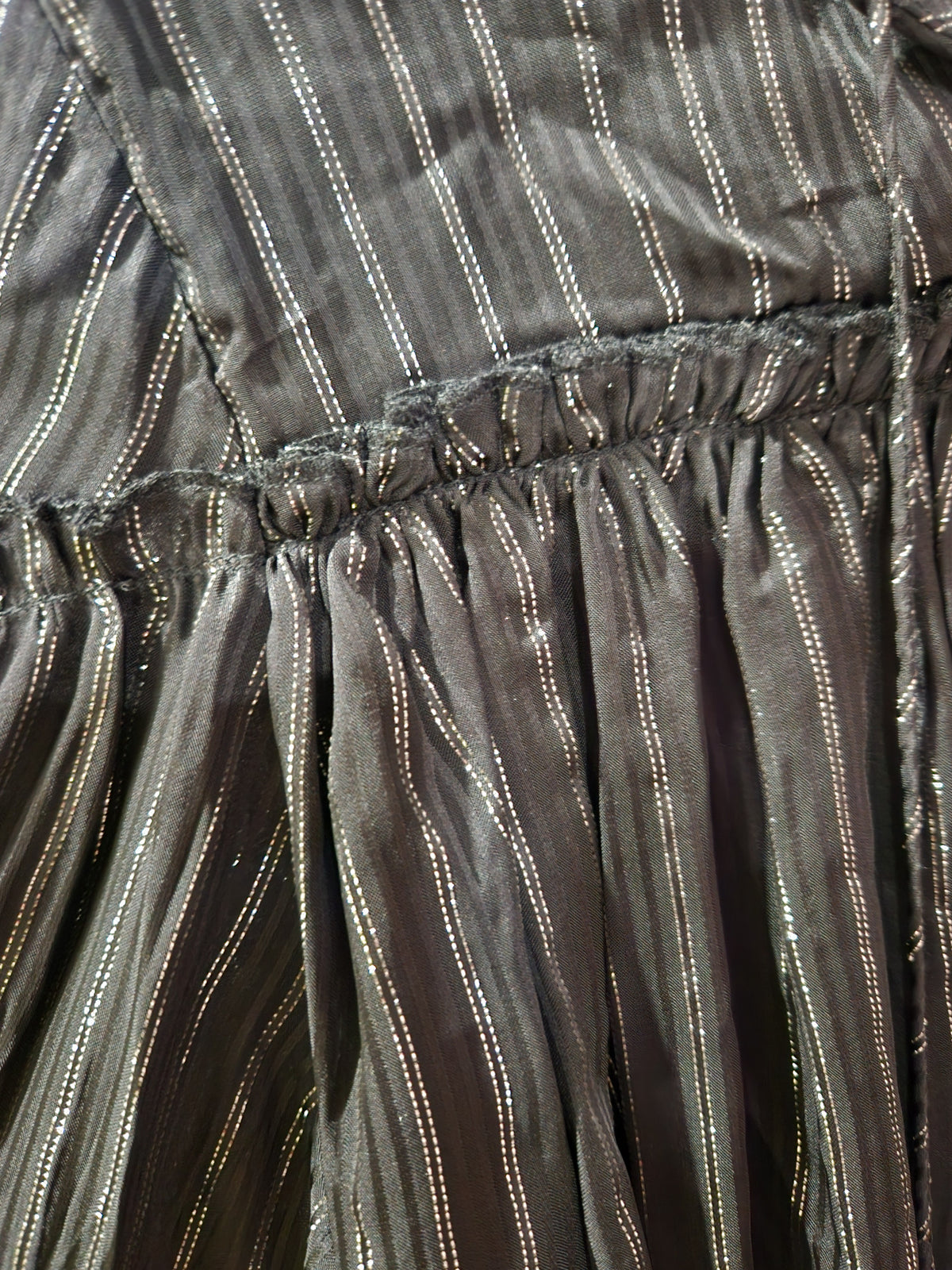 Close-up of a dark gray pleated fabric with vertical metallic gold stripes and a gathered waist seam.