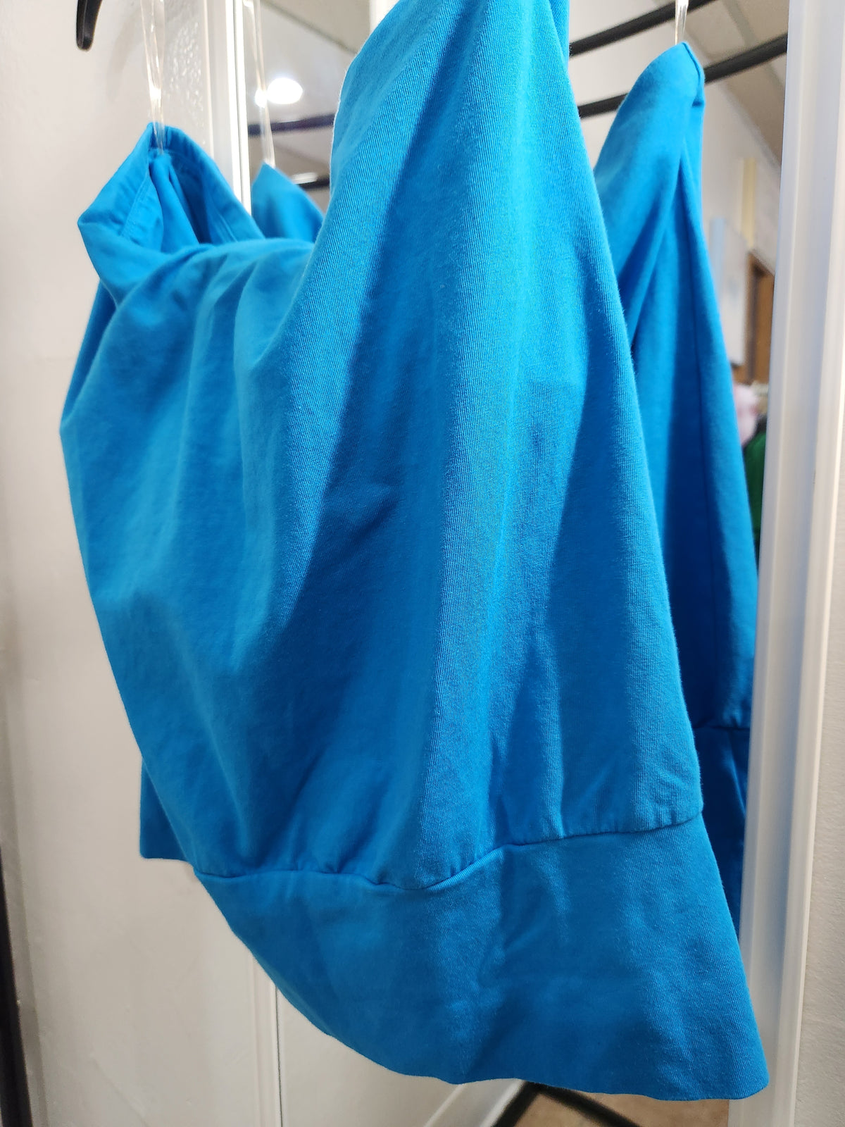 A bright blue scrub top or medical gown hanging on a hanger inside a closet or storage area.