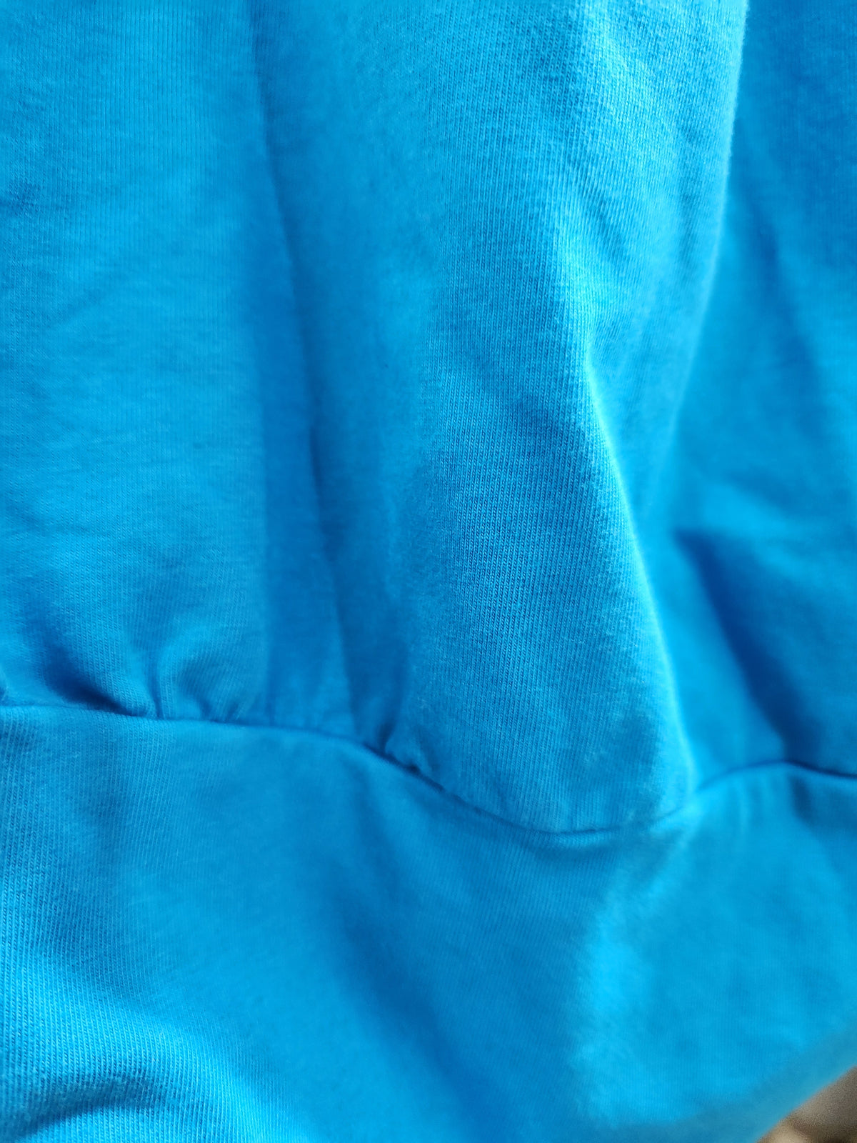A close-up of bright blue fabric with visible knit texture and a horizontal seam.
