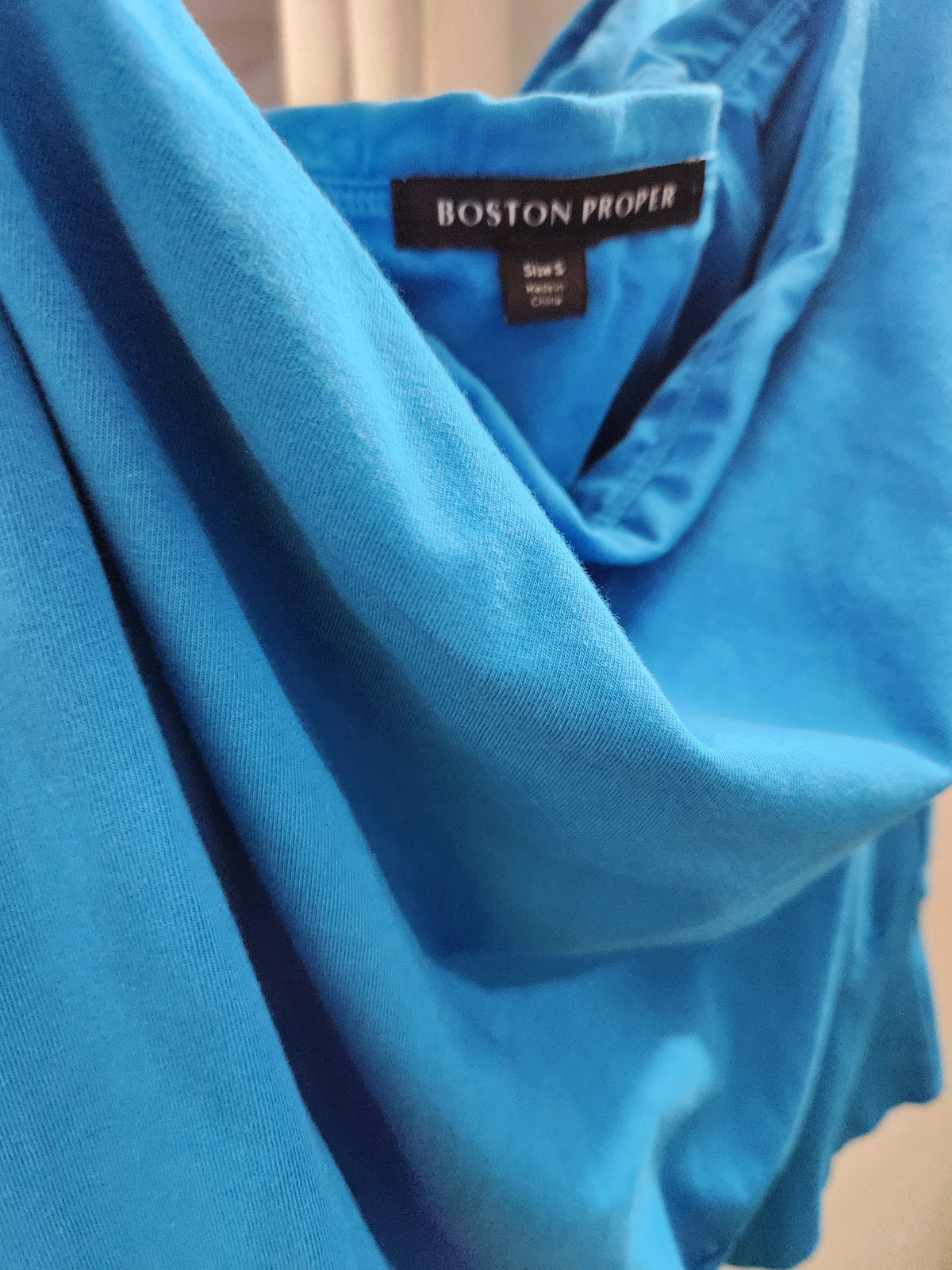 A close-up of a bright blue Boston Proper garment, showing the brand label inside the collar and the draped fabric texture.
