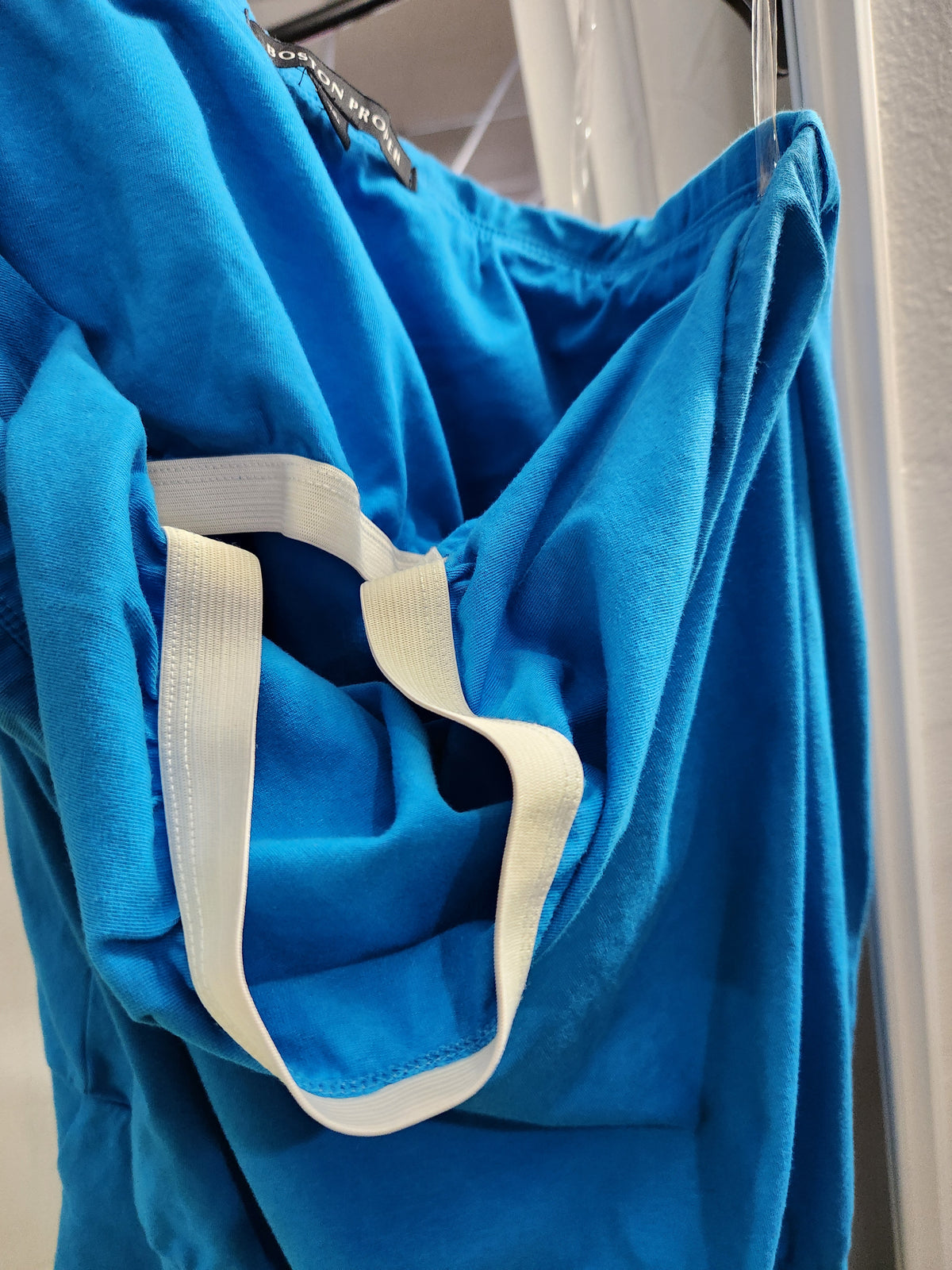 A bright blue fabric bag or pouch with white handles, hanging on a metal rack against a light-colored wall.