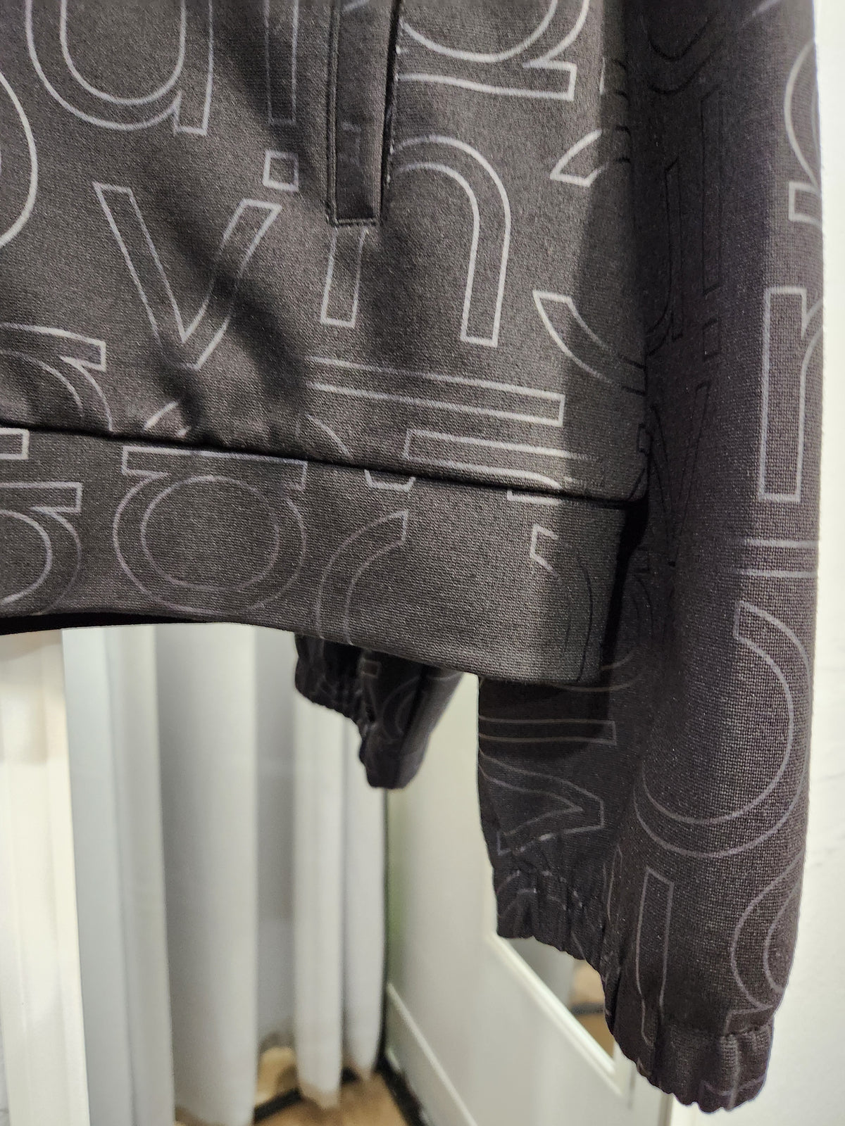Close-up of a dark gray long-sleeve top with a white outline geometric pattern, featuring a ribbed hem and elasticized cuffs.
