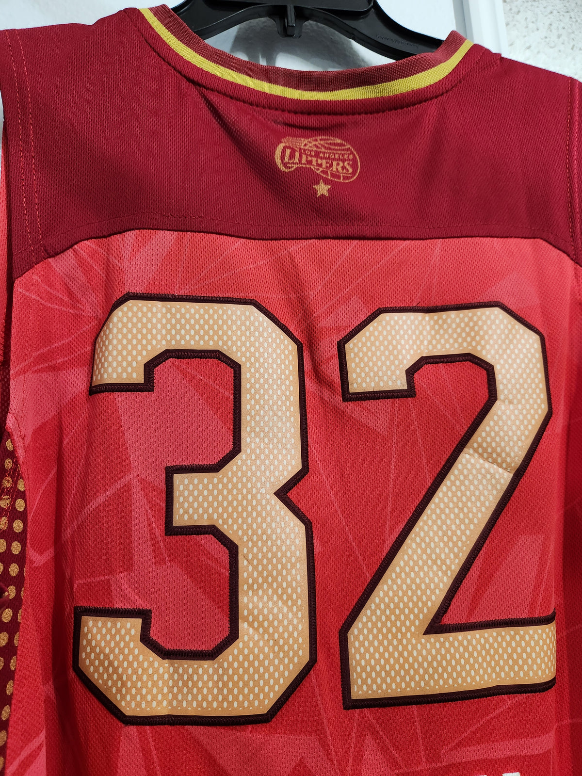 Close-up of the back of a red Cleveland Cavaliers jersey with the number 32 in tan and black, hanging on a black hanger.