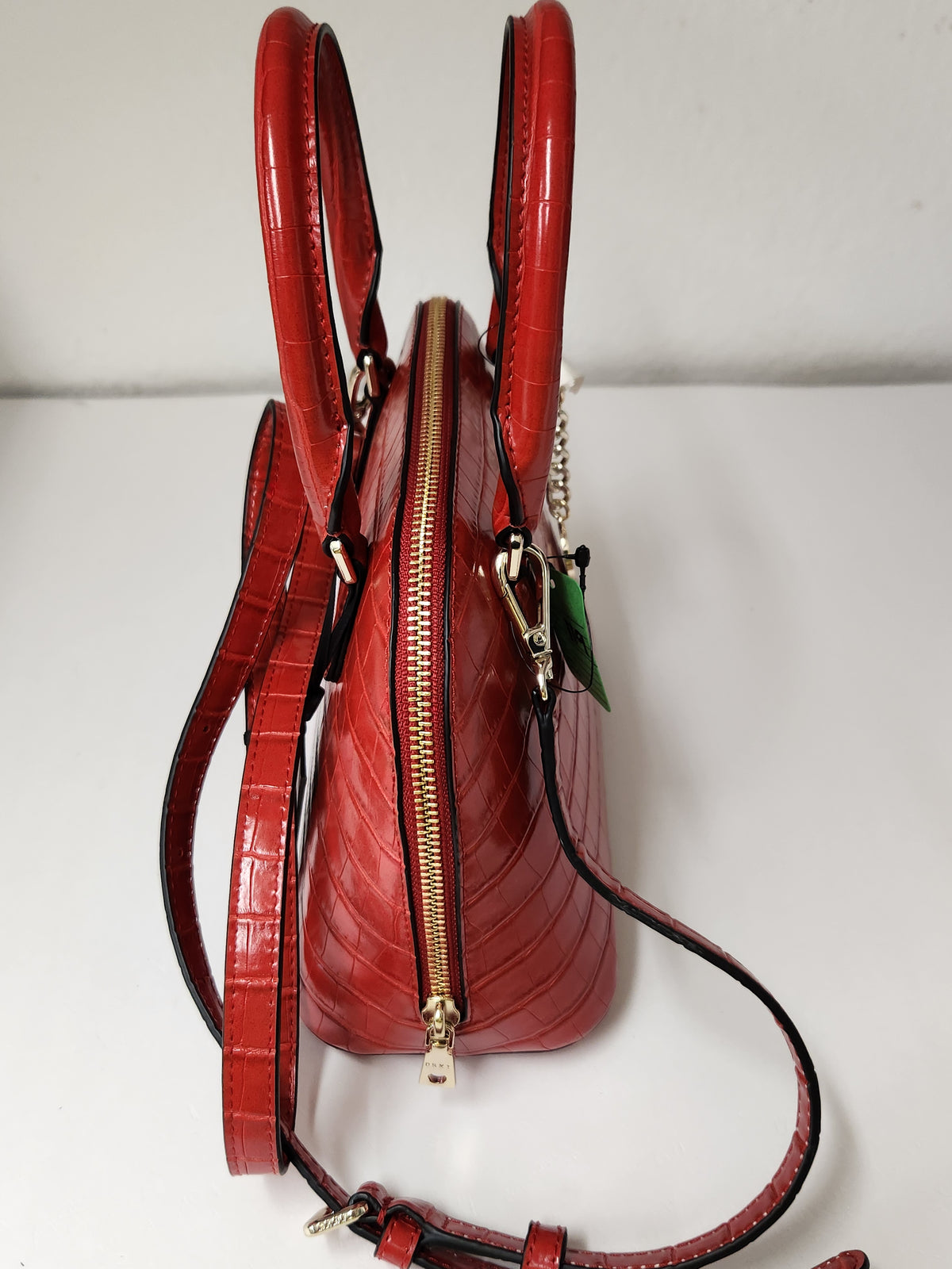 A red crocodile-embossed leather handbag with gold-tone hardware, featuring a zippered top closure, double top handles, and a detachable shoulder strap, photographed against a plain white background.