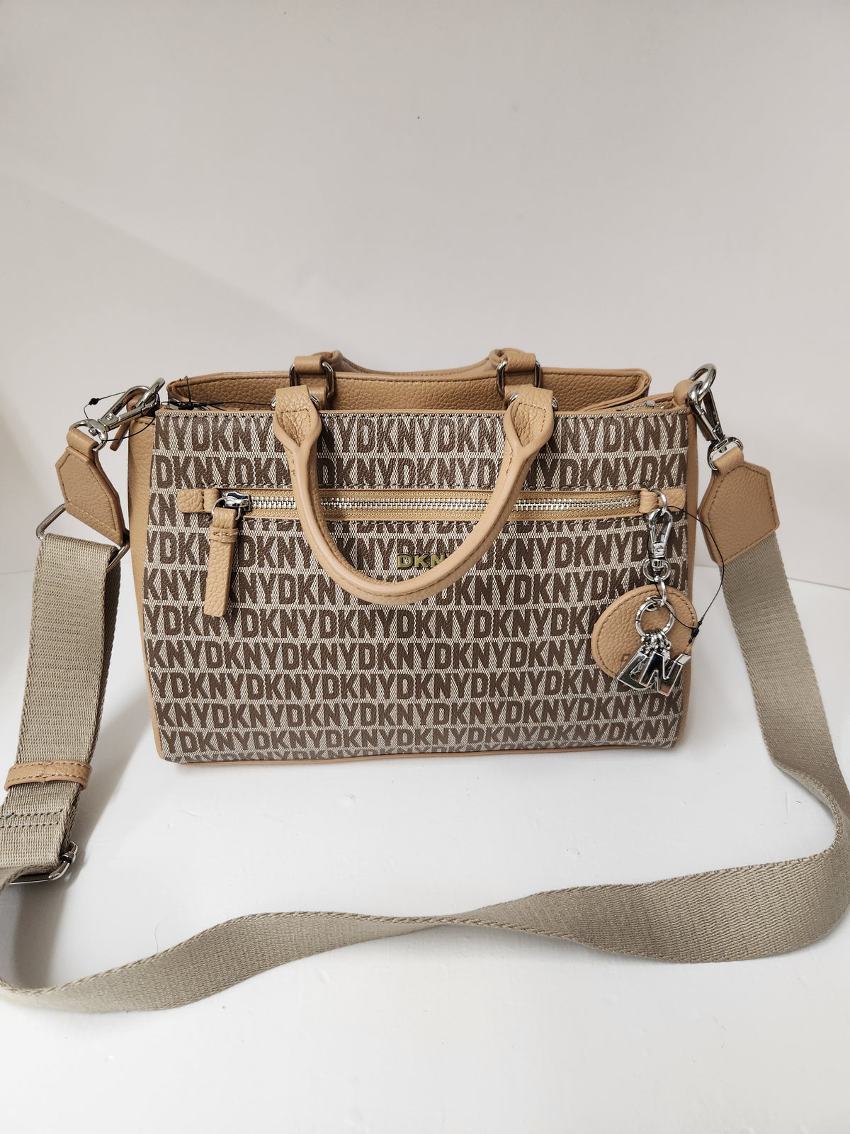 A beige and brown monogram handbag with a matching shoulder strap, top handles, and a hanging charm, displayed on a white background.